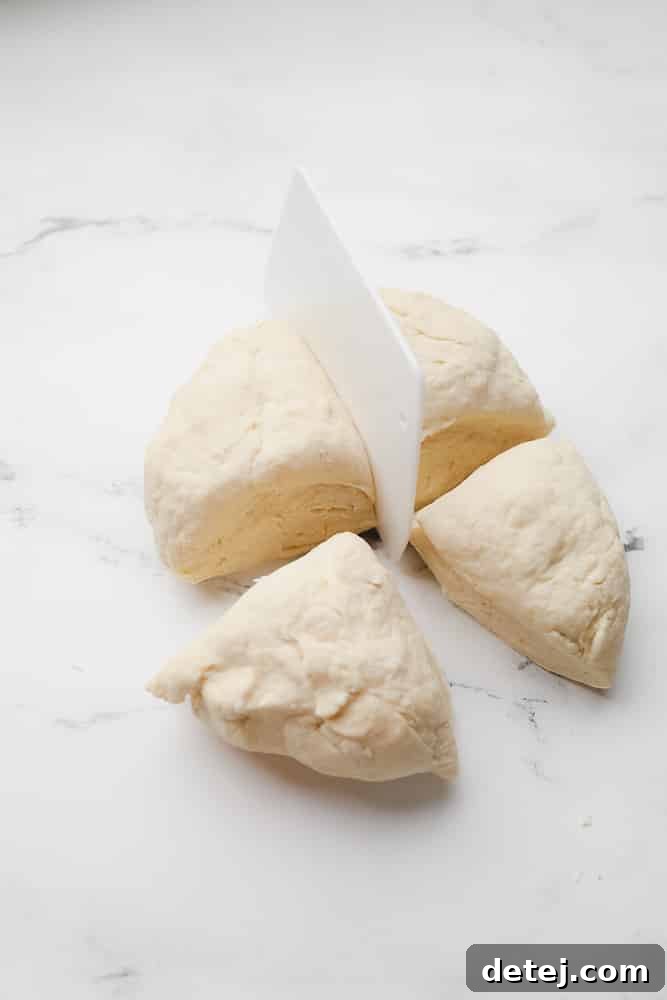 Dough being divided into four sections with a dough cutter on a white surface.