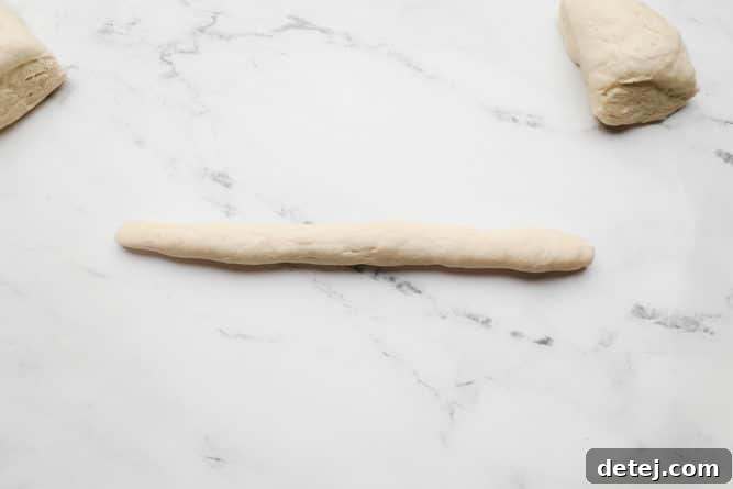 A long, evenly rolled log of dough resting on a white marble background.