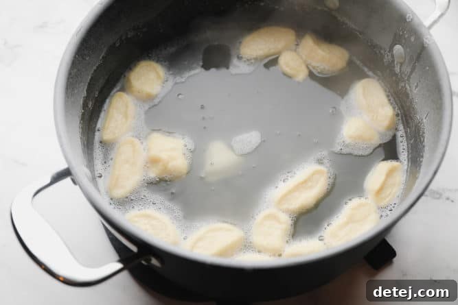 Dough pieces floating and boiling in a large pot containing a baking soda bath.