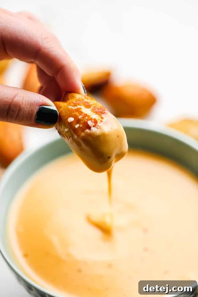 pretzel bite being dipped into cheese sauce, pulled out showing it dripping down into the bowl