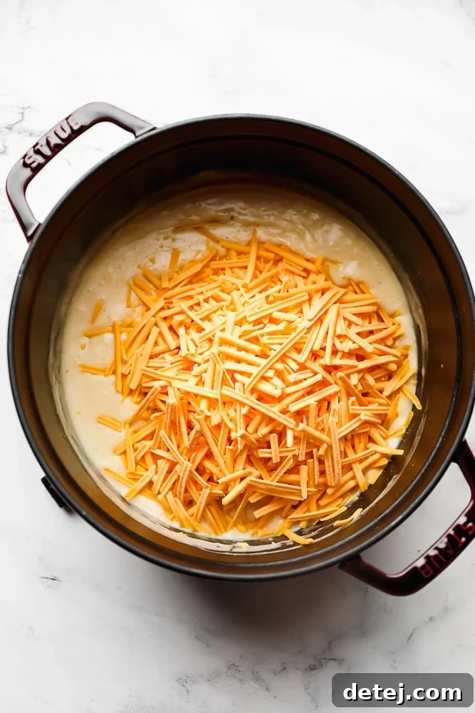 staub pot on white marble background, creamy sauce and shredded cheese added on top