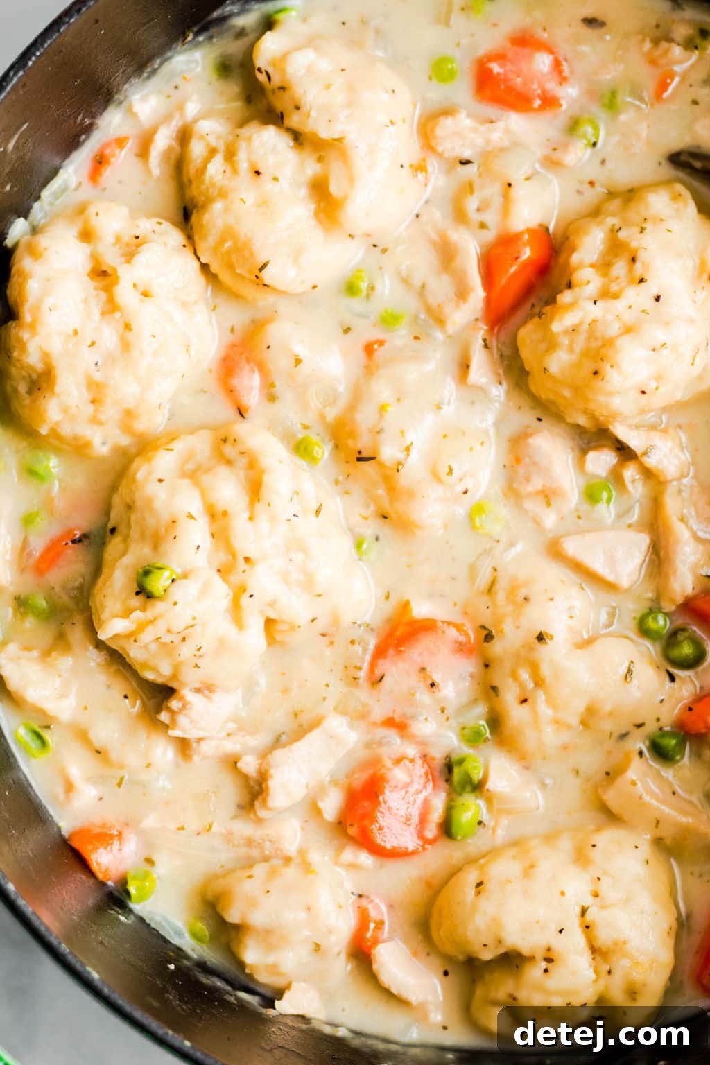 Close up shot of a large black pot filled with creamy vegan chicken and dumplings soup, highlighting the fluffy dumplings and rich broth.