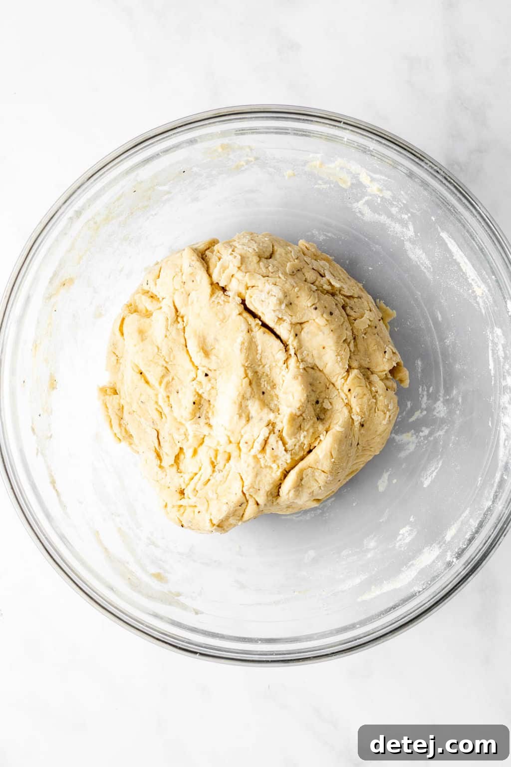 A perfectly rolled ball of smooth dough resting inside a glass bowl, indicating readiness for forming dumplings.