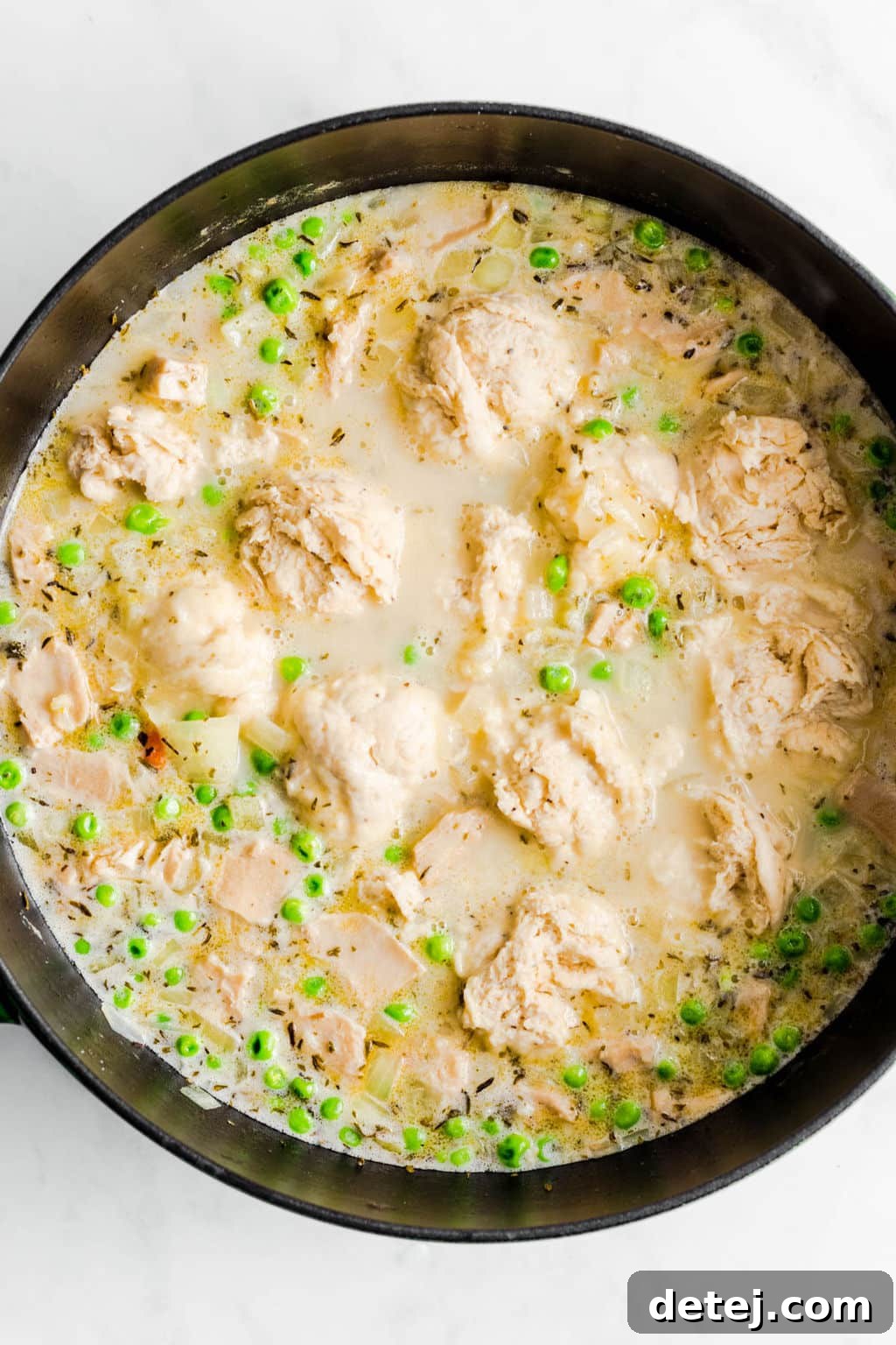 Raw dough dumplings gently cooking in a large black pot, submerged in the creamy vegan chicken soup, steam rising from the surface.