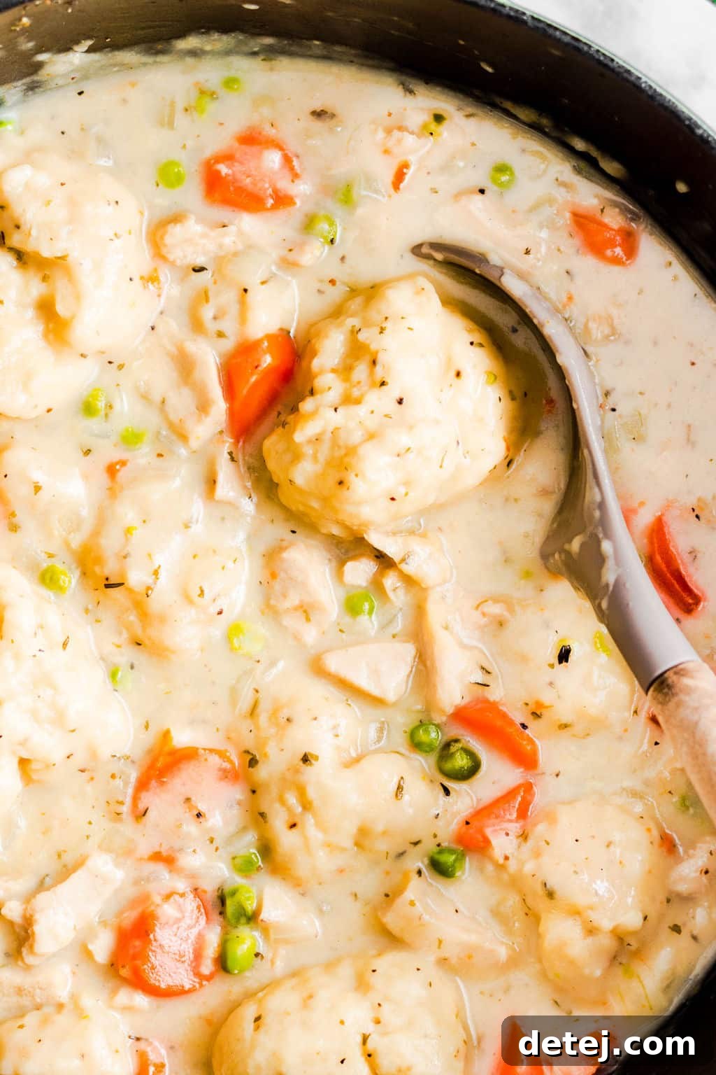 A large serving spoon gently scooping out a fluffy dumpling from a rich, creamy vegan chicken soup in a black pot, ready to be served.