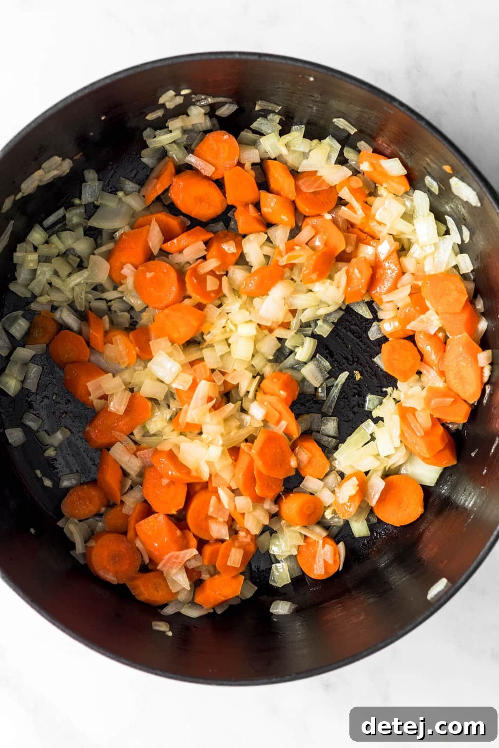 Carrots and onions being sautéed until softened in a large black pot on the stove.