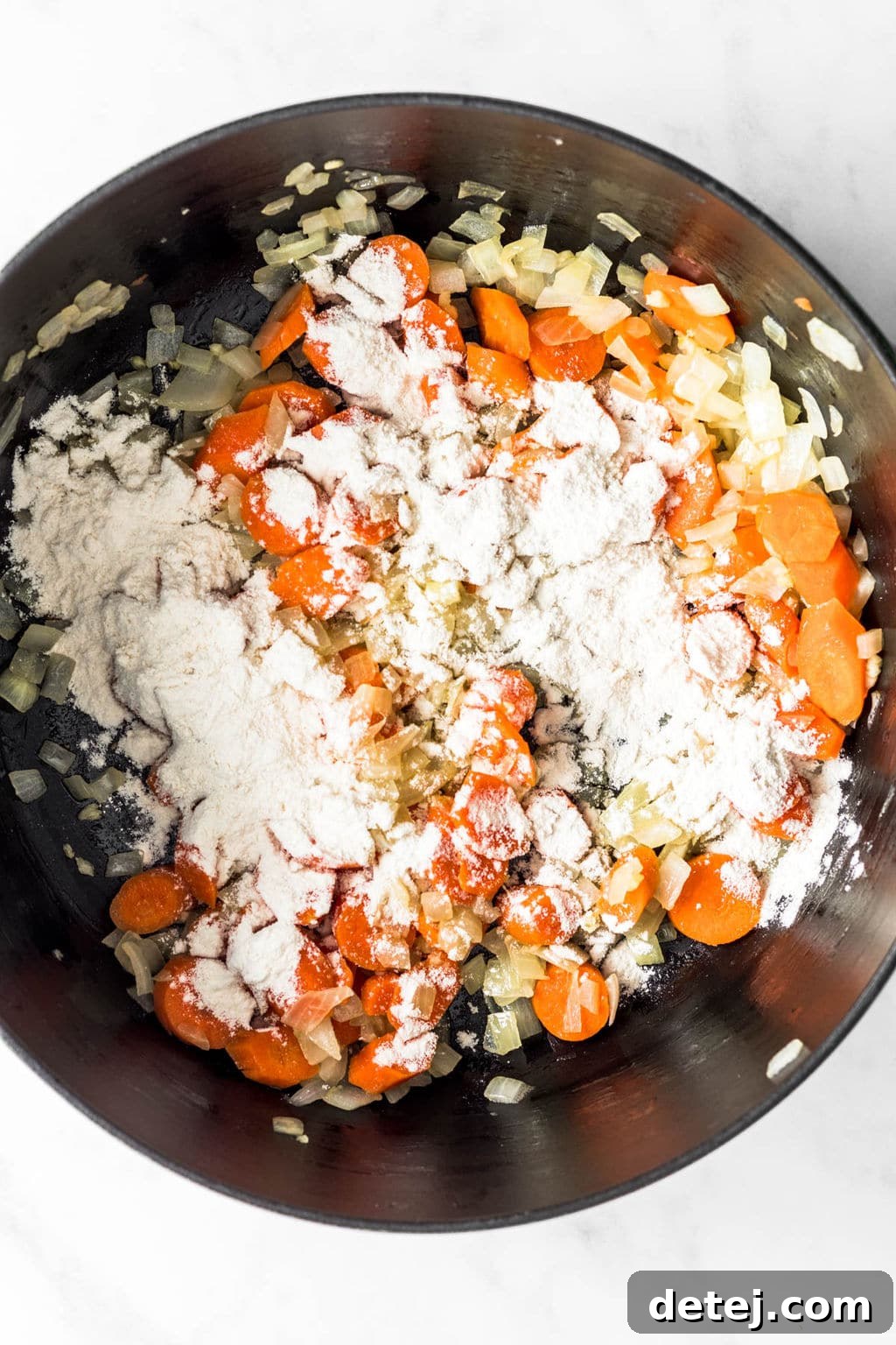 Sautéed carrots and onions coated in flour inside a large black pot, forming a roux.