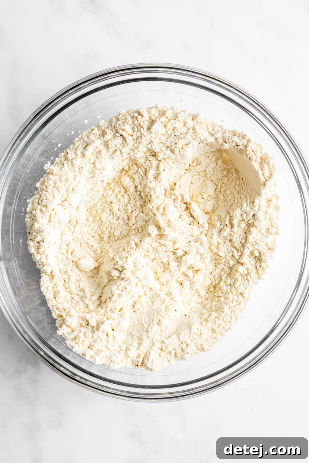 A large glass bowl containing a mound of all-purpose flour, ready for the dumpling dough preparation.