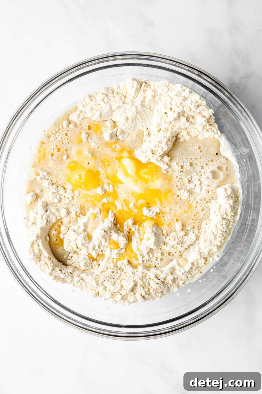 A large glass bowl holding flour with a well in the center, into which melted vegan butter and plant milk have been added, ready for mixing.