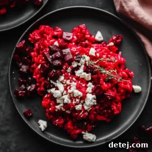 Close-up of a black plate with vibrant red beetroot risotto, topped with vegan cheese and roasted beet cubes.