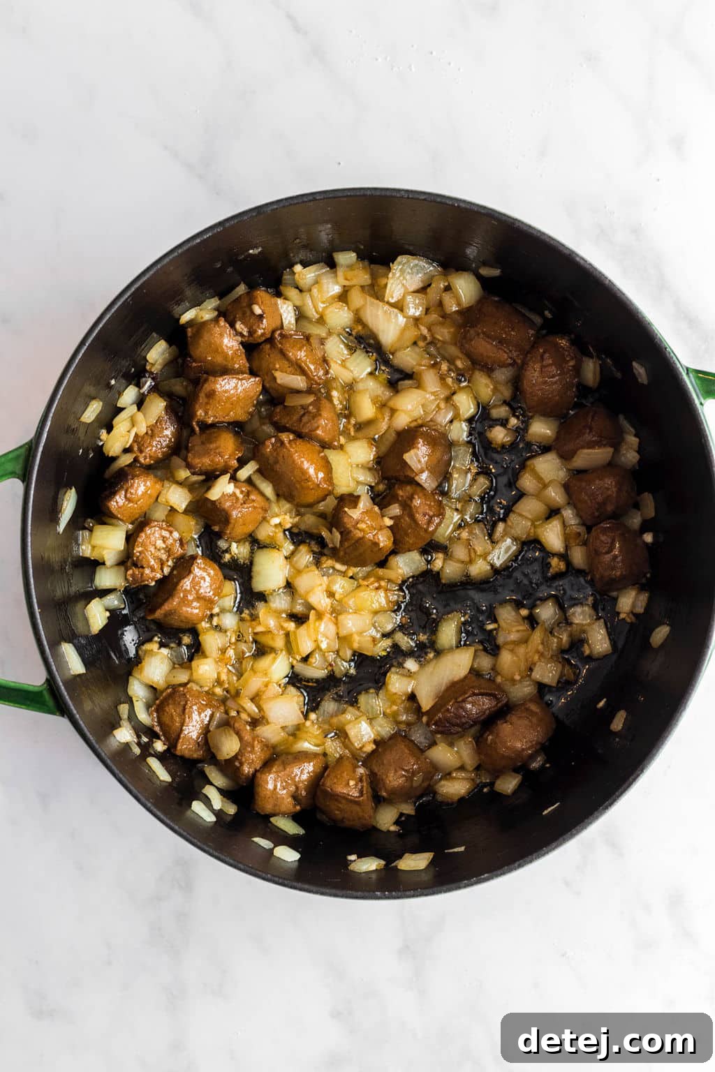 Sautéing chopped onions and vegan sausage (or beefless tips) in a large black skillet, illustrating the initial cooking step.