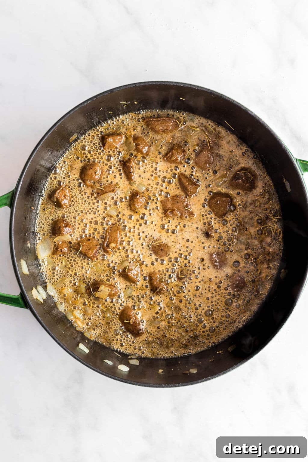 A large black skillet with a sauce and vegan sausage (or beefless tips) simmering, showing the broth development stage.