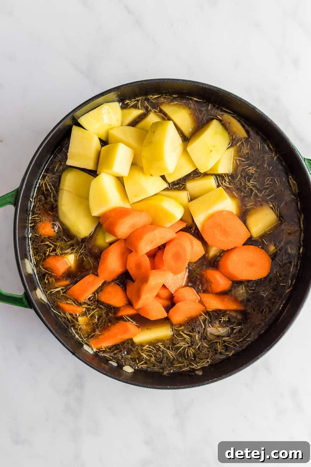 Close-up of potatoes and carrots cooking in a large pot with broth, illustrating the simmering process of the stew.
