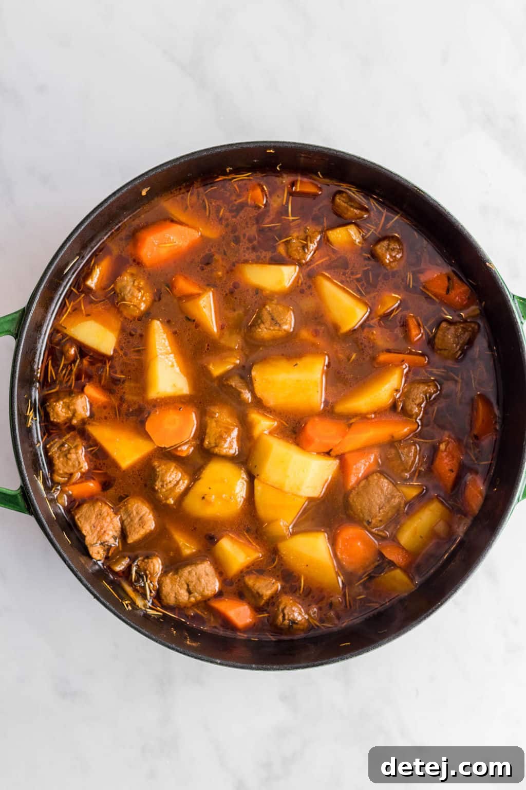 A large pot of vegan Irish stew simmering on a stovetop, showing the rich, dark broth and tender vegetables.