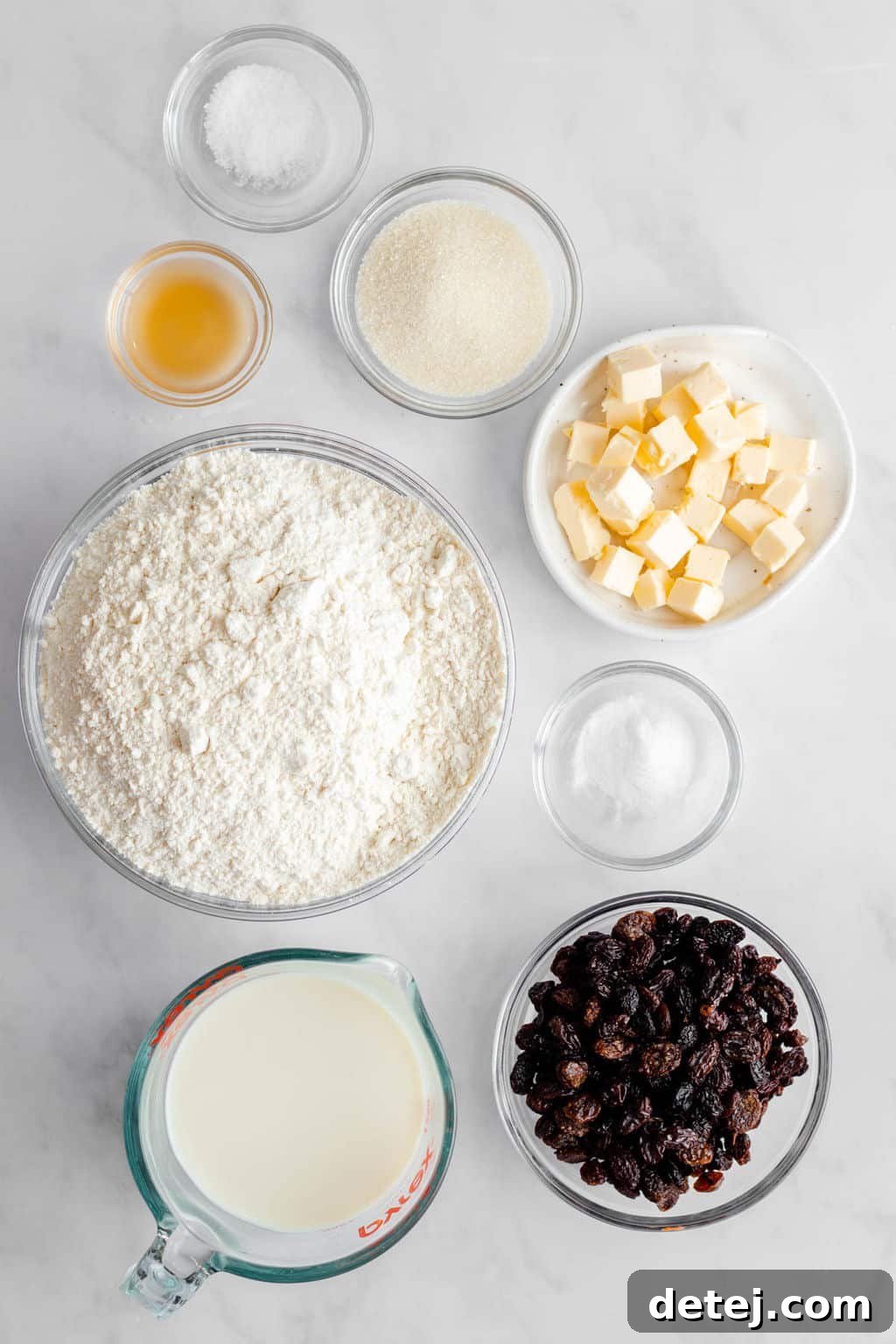 Individual glass bowls filled with ingredients for vegan Irish soda bread: soy milk, vinegar, flour, sugar, baking soda, salt, vegan butter, and raisins.