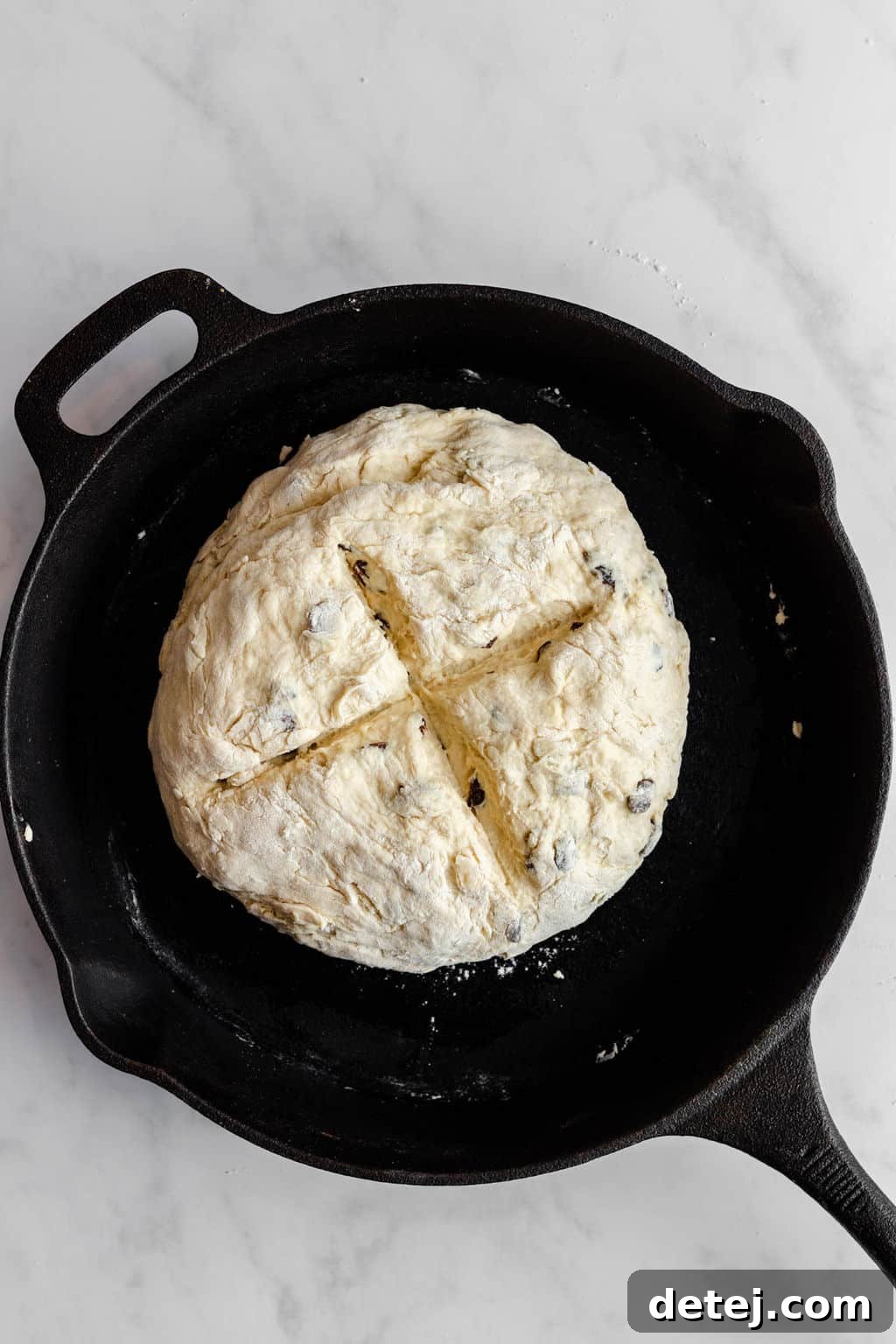 A perfectly scored ball of vegan Irish soda bread dough resting in a black cast iron pan, ready for baking.