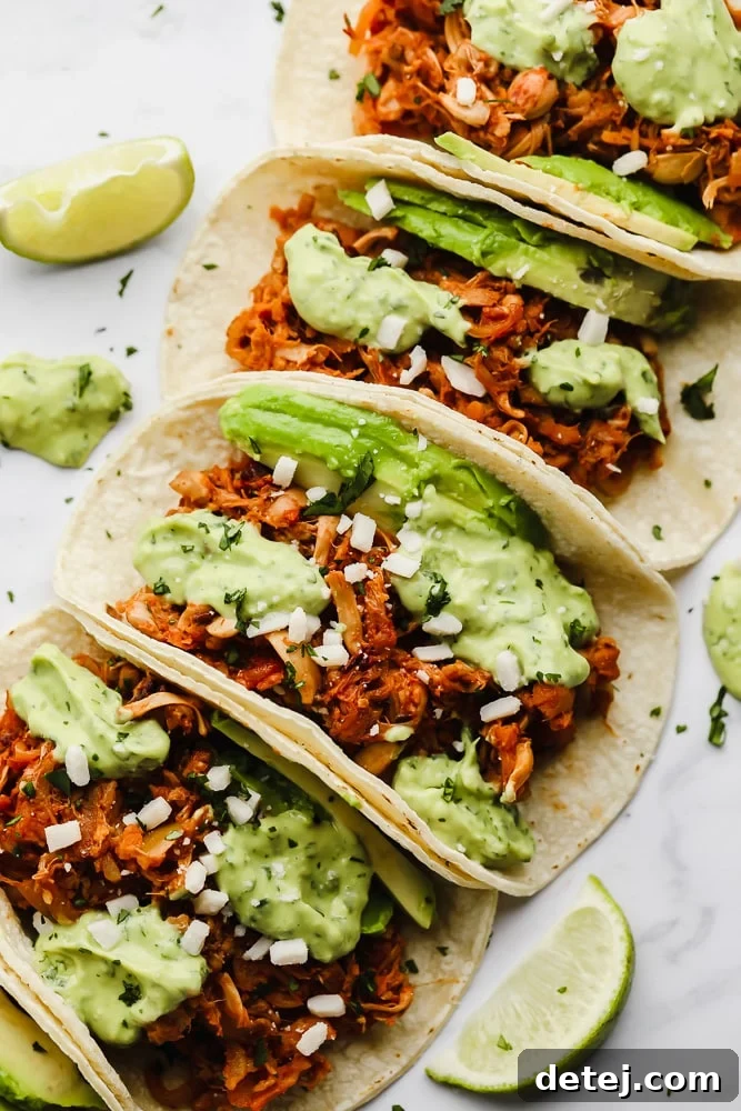 Pulled Jackfruit Tacos 2 jackfruit tacos topped with a green avocado sauce lined up in a row.