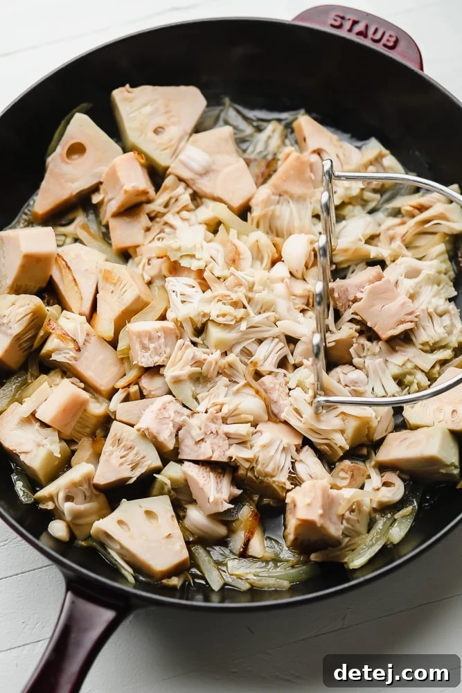 Pulled Jackfruit Tacos 4 mashing jackfruit in a black skillet with a potato masher.