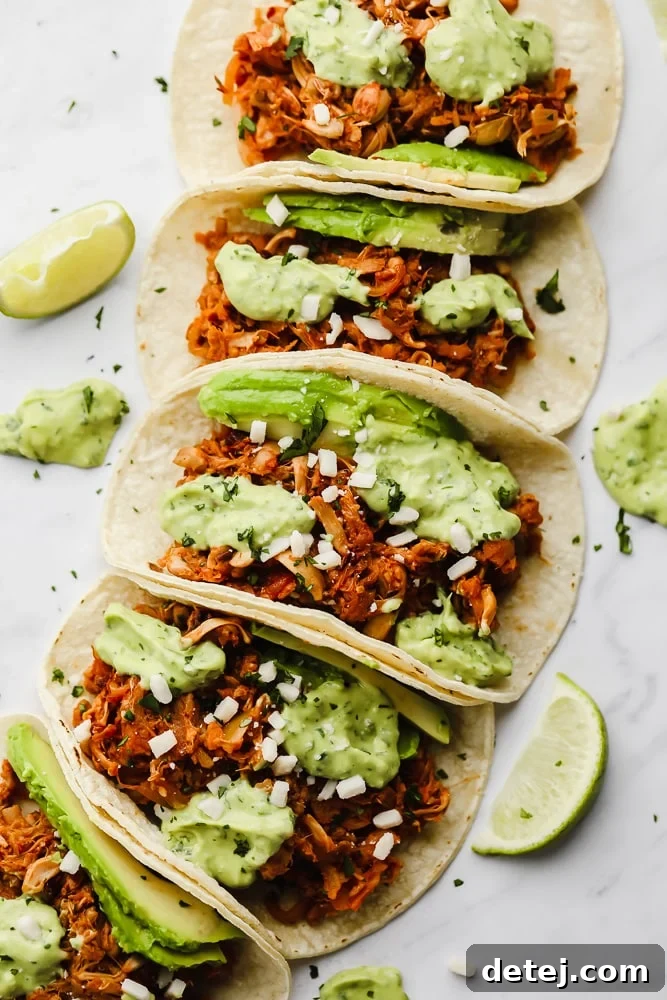 Pulled Jackfruit Tacos 8 jackfruit tacos topped with a green avocado sauce lined up in a row.