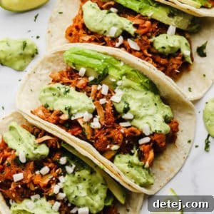 Pulled Jackfruit Tacos 9 close up on jackfruit tacos topped with a green avocado sauce lined up in a row.