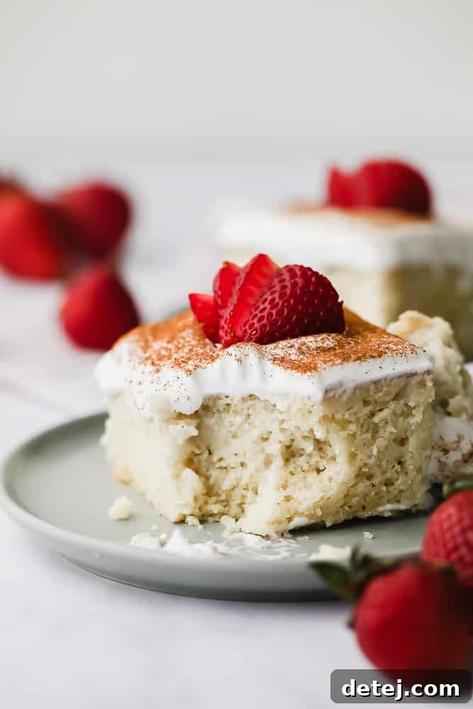 A beautifully presented yellow vegan tres leches cake, generously topped with white frosting and fresh, vibrant sliced strawberries.