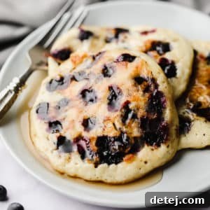 Three perfectly stacked vegan blueberry pancakes on a white plate, ready for a delicious breakfast.