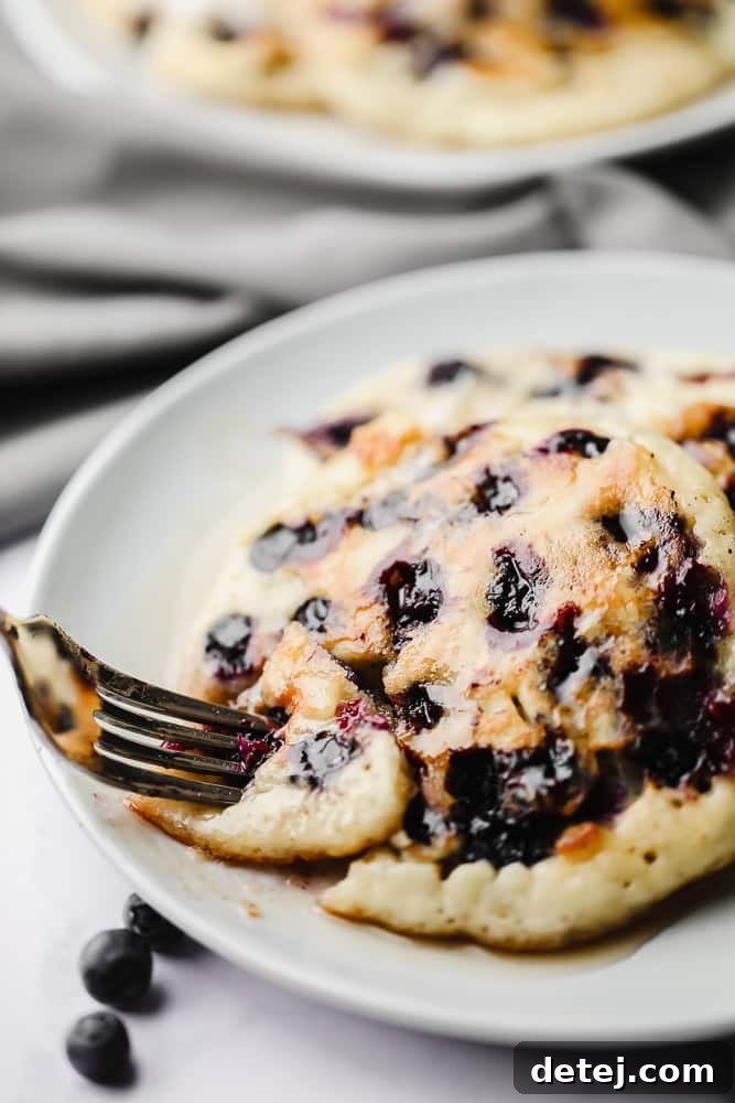 A fork piercing into a stack of fluffy vegan blueberry pancakes, showcasing their tender interior and juicy blueberries.