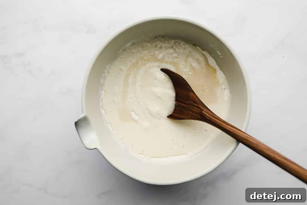 A wooden spoon gently stirring thick vegan pancake batter in a white bowl, showing the perfect consistency before adding blueberries.