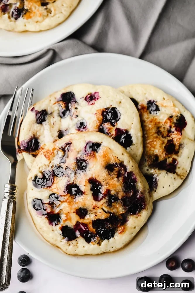 Another enticing shot of three soft, thick vegan blueberry pancakes piled on a white plate, inviting you to take a bite.