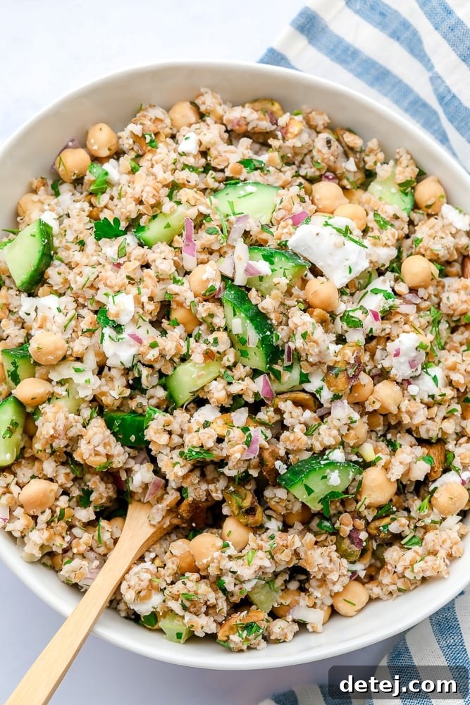 close up photo of a bowl of grain salad with wooden spoon and blue striped towel