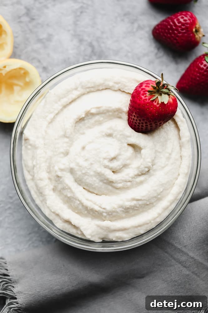 A bowl filled with creamy white vegan mascarpone, garnished with fresh strawberries, set against a stylish grey background.
