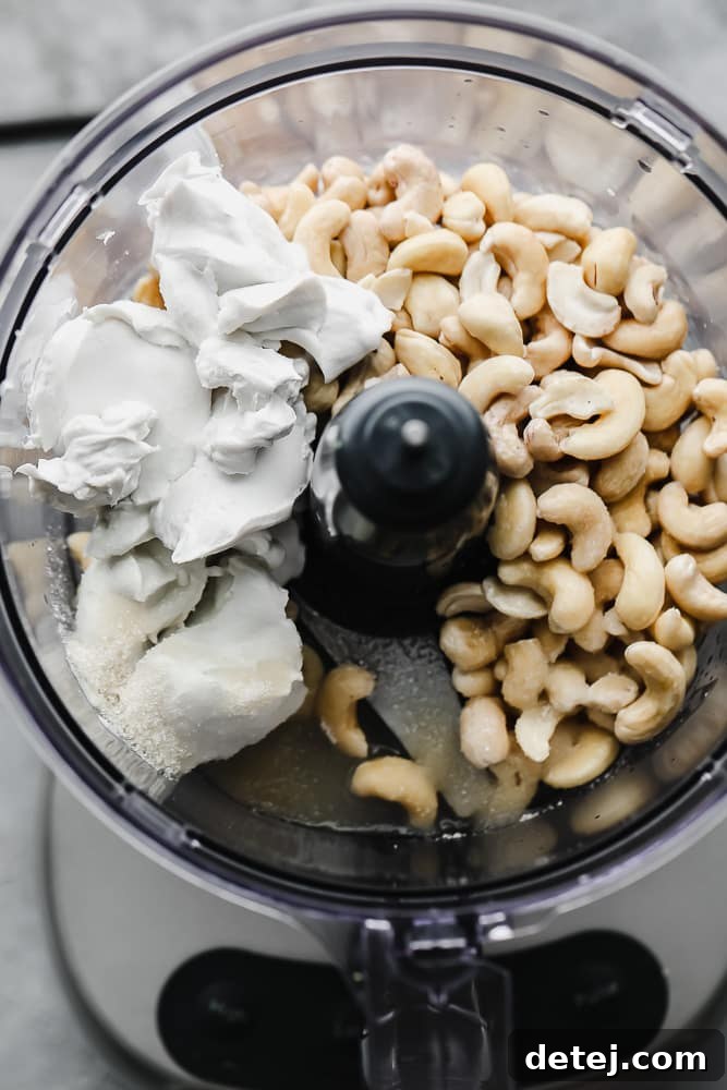 A food processor bowl containing soaked cashews, coconut cream, and sugar, ready for blending into vegan mascarpone.