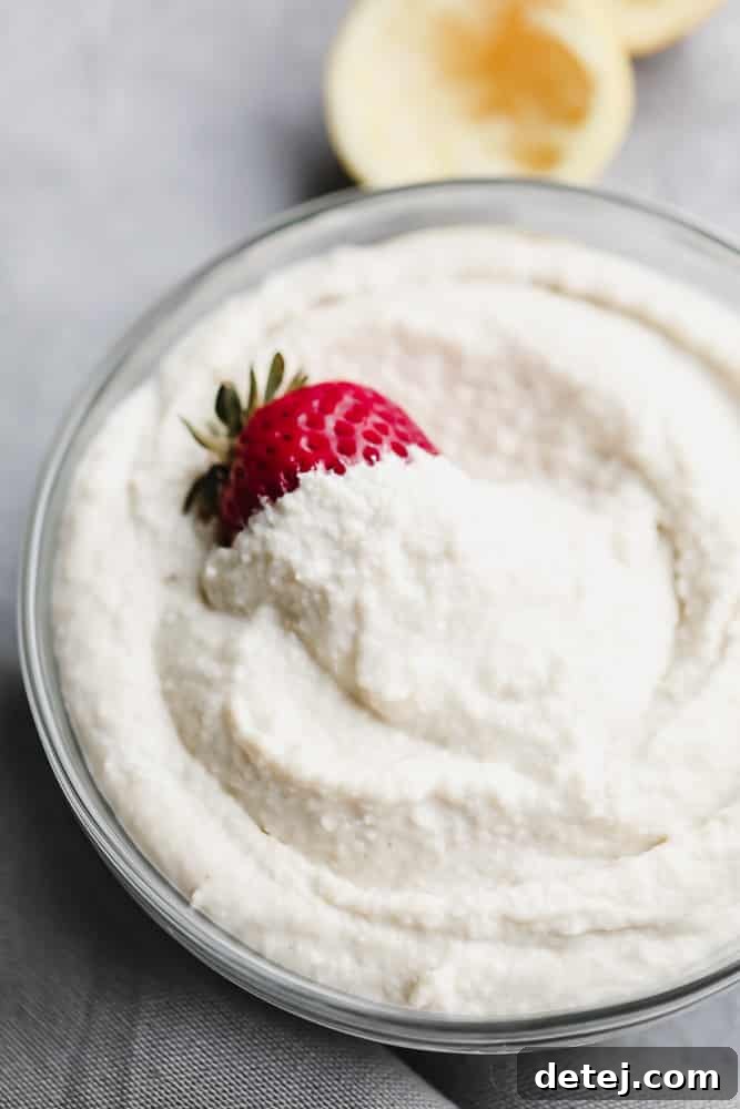 A elegant glass bowl filled with the creamy white vegan mascarpone cheese, adorned with a single ripe strawberry, on a contrasting grey background.