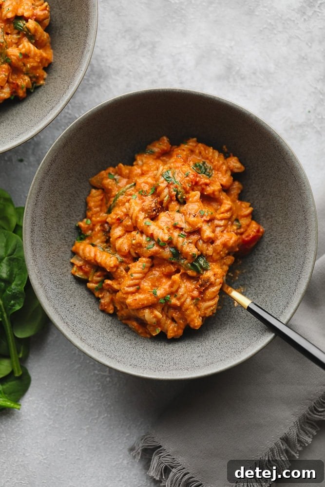 A grey bowl filled with perfectly cooked vegan tomato sauce-covered pasta, garnished with fresh herbs, ready to be enjoyed.