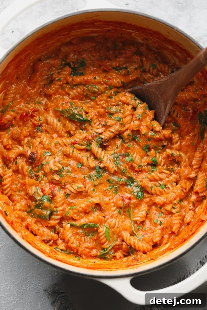 A wooden spoon gently stirs vibrant vegan tomato sauce-covered pasta in a large white pot, steam gently rising.