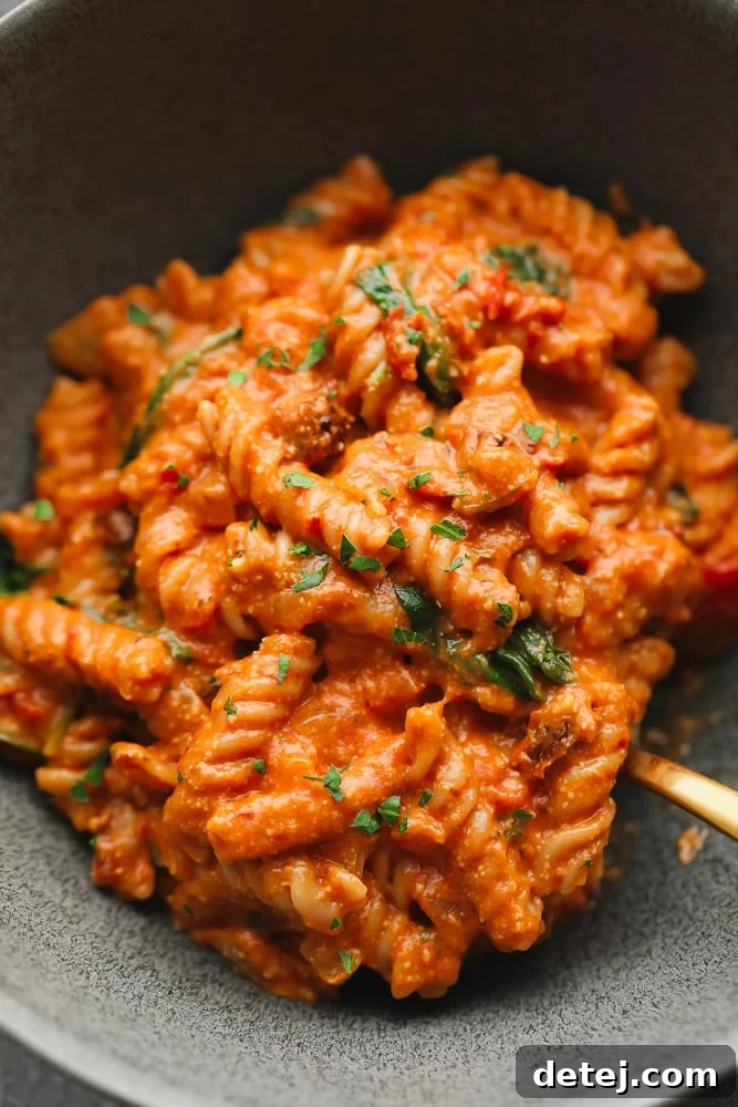 A close-up shot of vegan tomato sauce-covered pasta in a grey bowl, highlighting its creamy texture and rich color.
