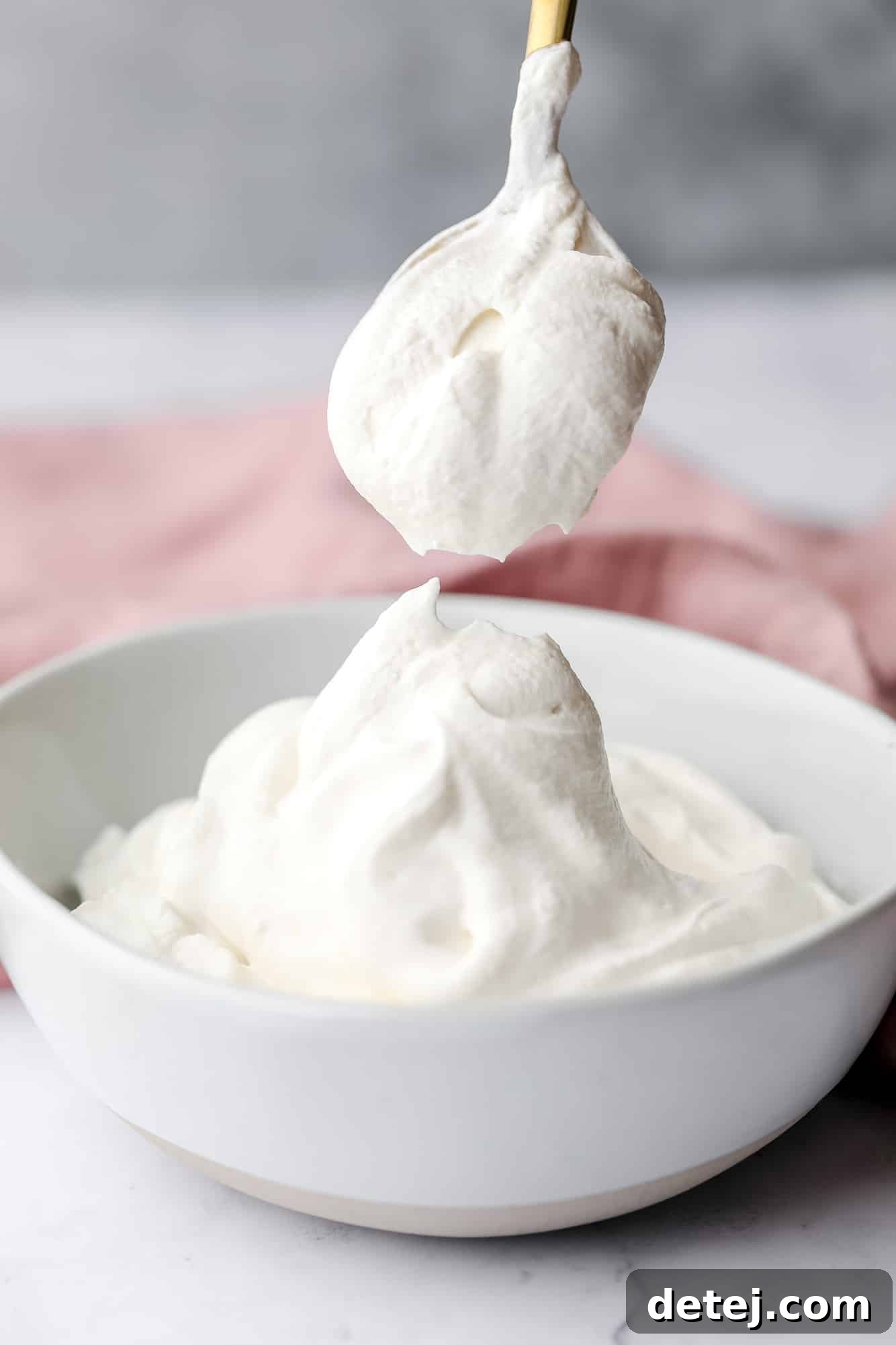 a spoon scooping a dollop of vegan whipped cream out of a white bowl.