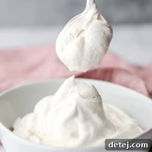 a spoon scooping a dollop of vegan whipped cream out of a white bowl.