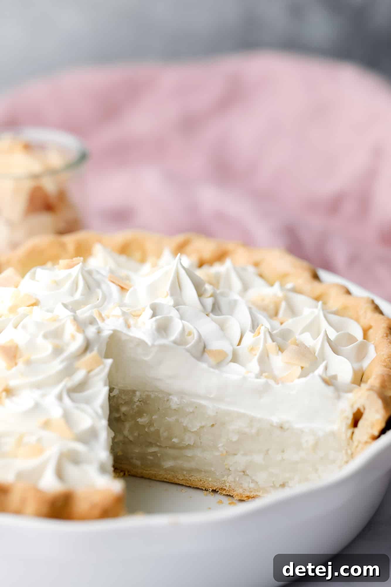 A beautifully presented vegan coconut cream pie in a white pie plate, with a perfect slice removed to showcase its creamy layers.