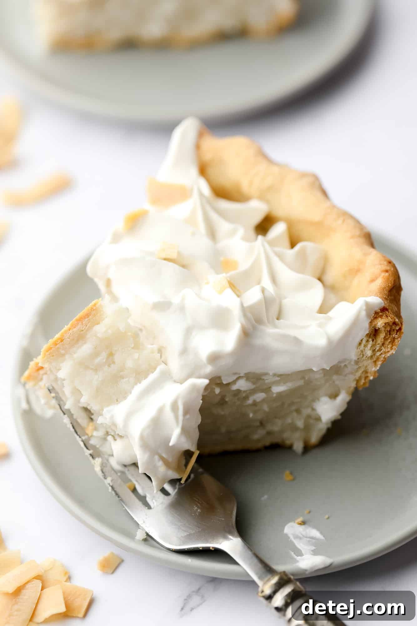 A tantalizing close-up of a fork taking a bite out of a fresh slice of vegan coconut cream pie, showing its smooth custard and fluffy whipped topping.