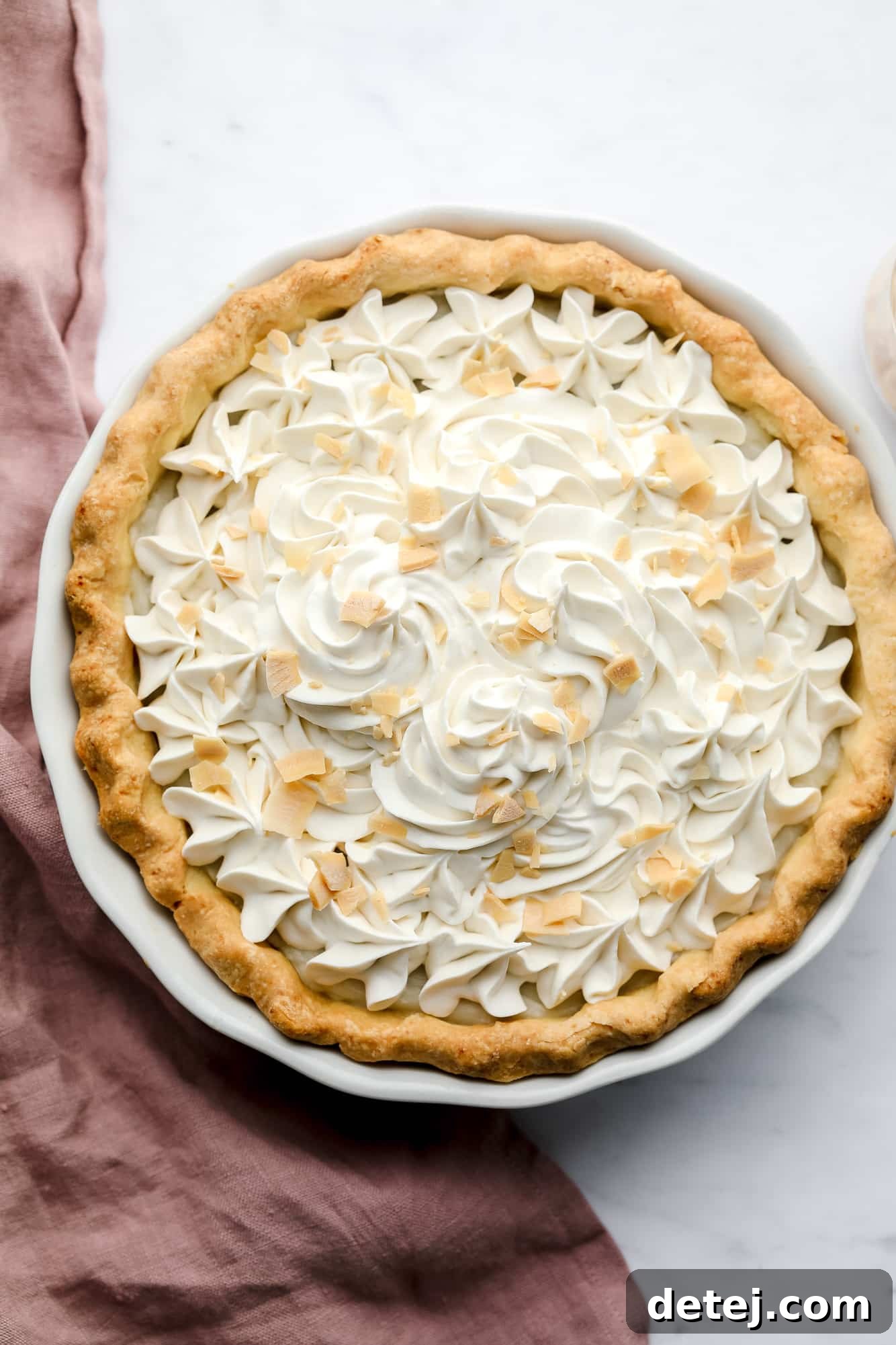 A whole baked vegan coconut cream pie, generously topped with fluffy vegan whipped cream and golden toasted coconut shreds.