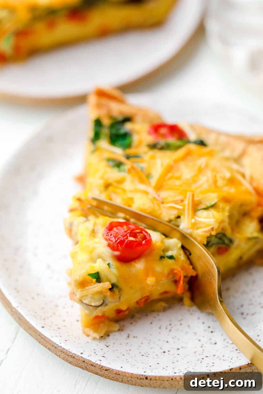 A fork taking a delicious bite out of a slice of warm JUST Egg quiche, showcasing the creamy filling and vibrant vegetables. Perfect for a vegan breakfast.