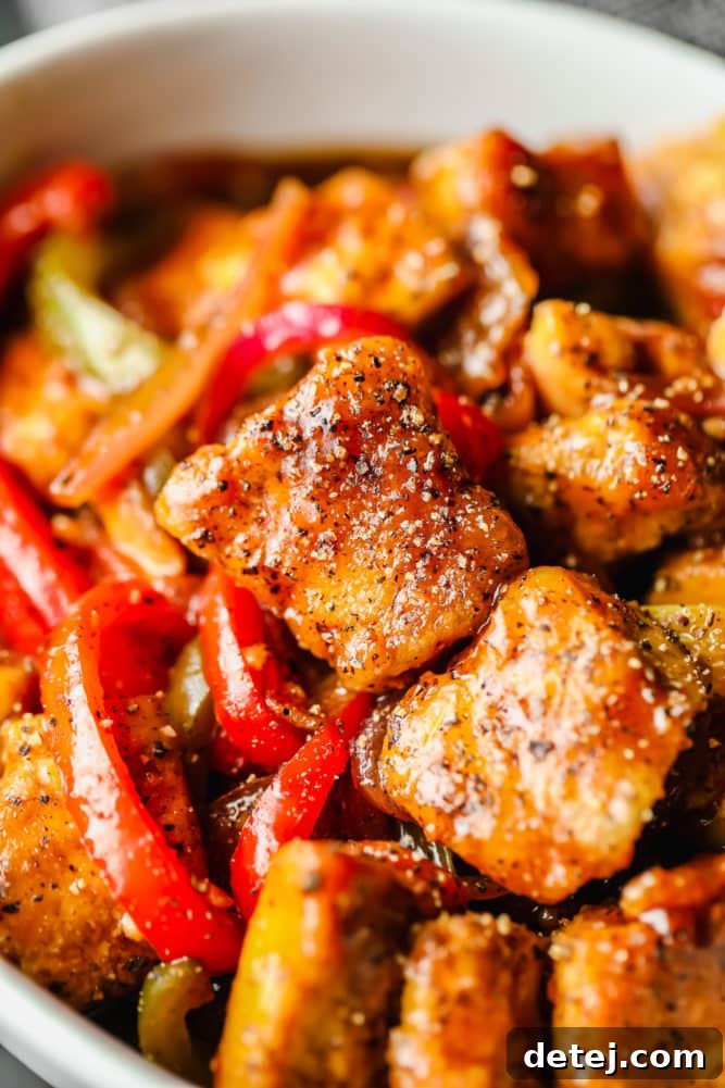 Close-up of golden, crispy cooked tofu and colorful bell peppers generously coated in a dark, peppery sauce, showcasing the rich texture and seasoning.