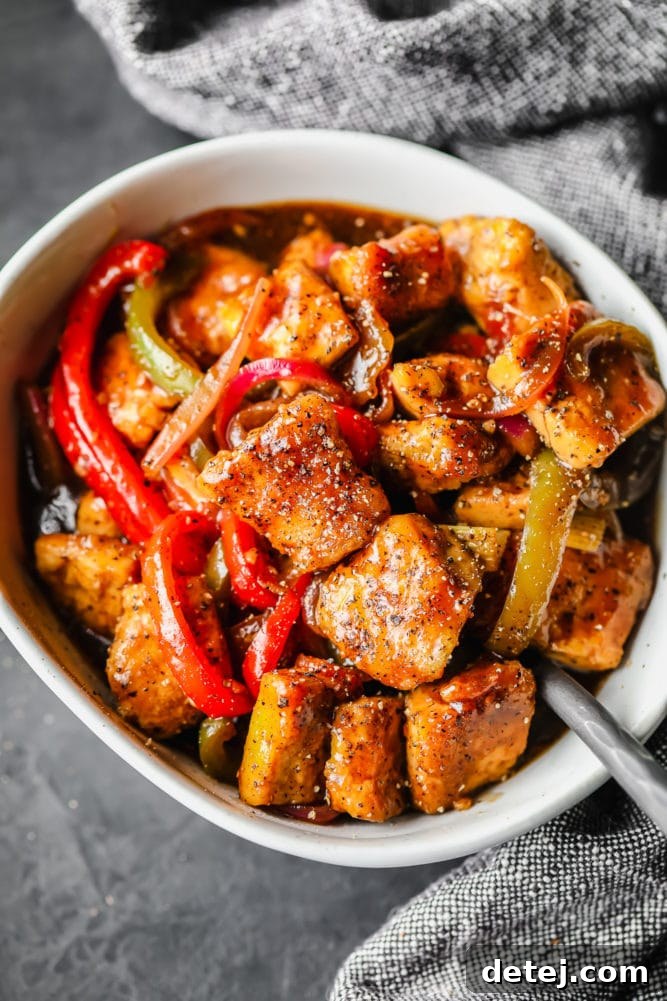 A beautifully presented white bowl filled with Black Pepper Tofu and colorful peppers, set against a dark grey background with a textured towel, highlighting its appetizing appeal.