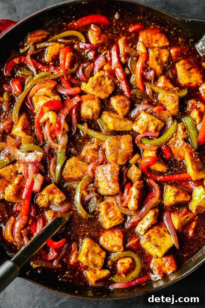 A top-down view of a pan brimming with Black Pepper Tofu, bell peppers, and onions, all coated in a rich, dark sauce, ready to be served.