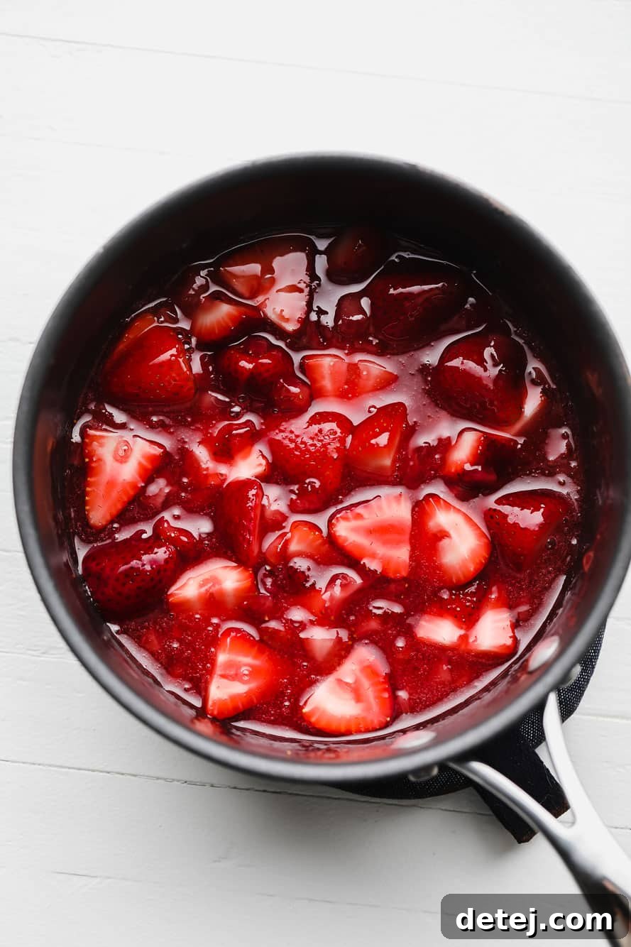 A saucepan filled with fresh strawberries, sugar, and water, simmering gently to create a rich strawberry sauce.