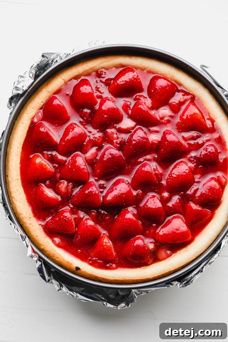 A stunning vegan cheesecake topped with vibrant strawberry sauce, still in its springform pan, ready for slicing.
