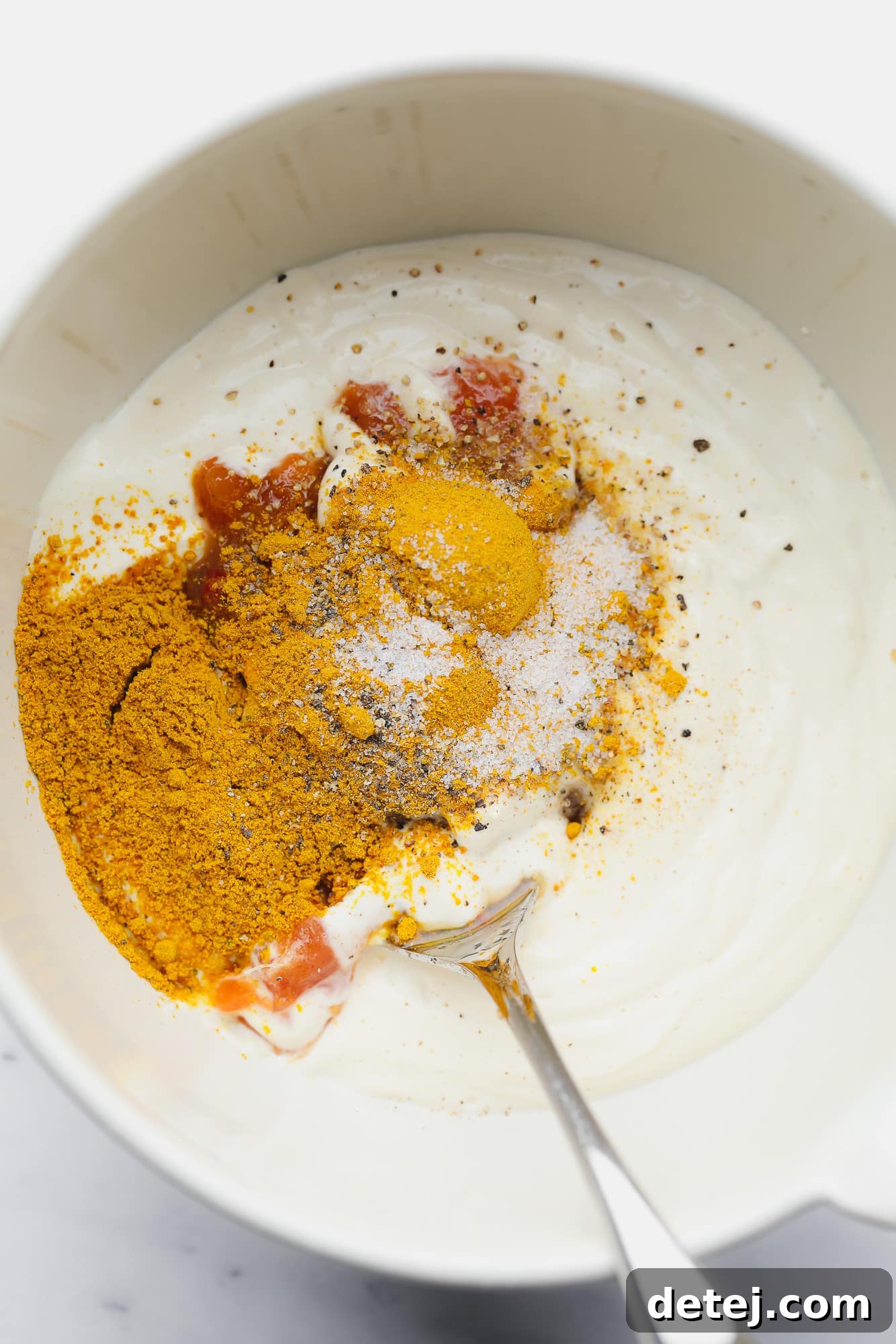 Golden Curried Tofu Salad 5 using a spoon to stir yellow and red spices into vegan mayonnaise in a white bowl.