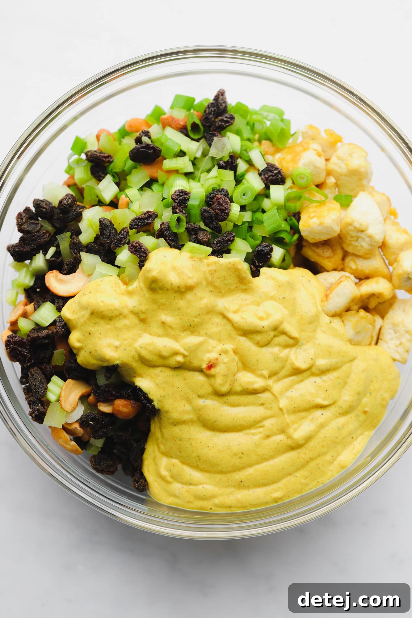 Golden Curried Tofu Salad 6 vegetables, baked tofu, and a creamy yellow sauce together in a large glass bowl.