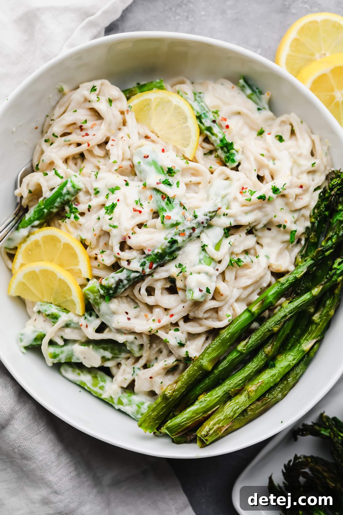 A beautiful bowl of creamy vegan lemon asparagus pasta, garnished with fresh asparagus spears and lemon slices.